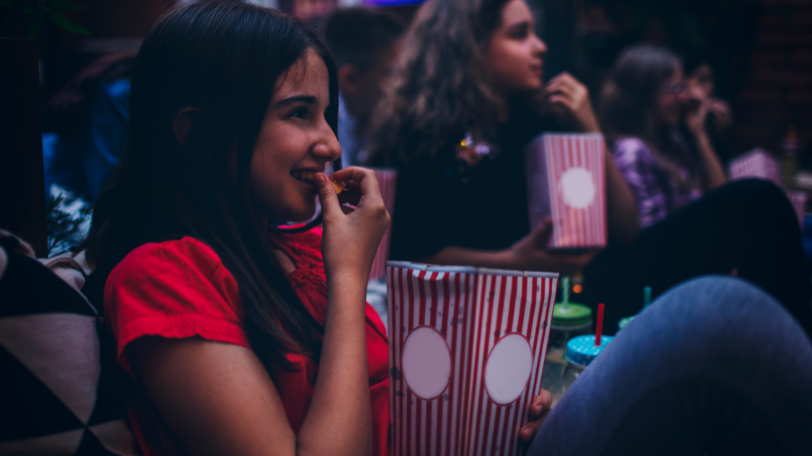 Young girl watching a movie with friends and eating popcorn.