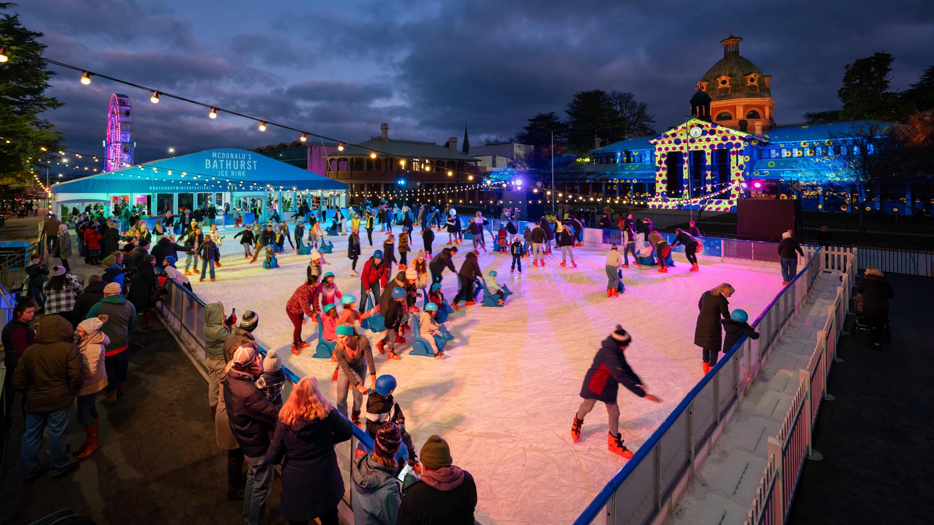 People skating on the McDonald's Bathurst Ice Rink at night with the illuminated Bathurst Courthouse in the background.