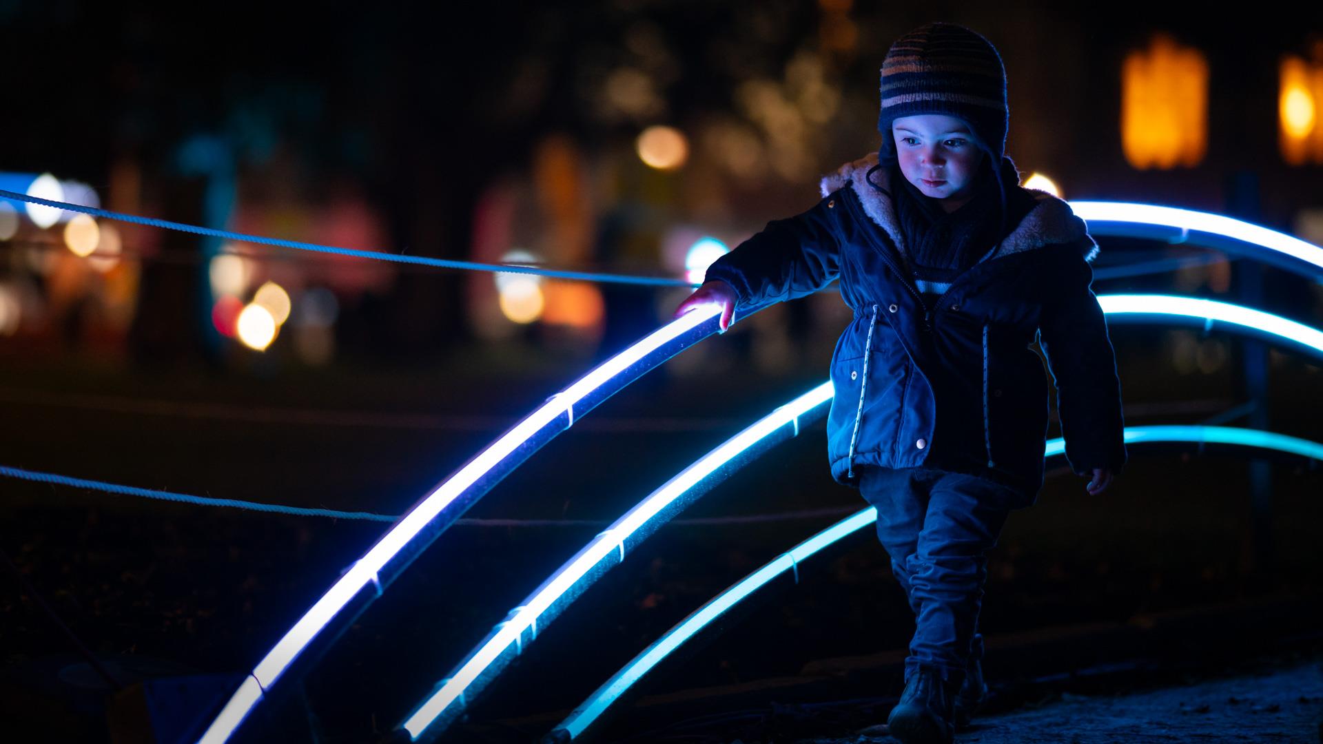 Young boy walking along footpath next illuminated rainbow.