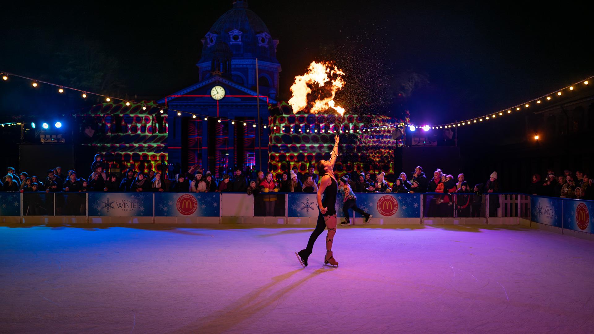 Professional ice skating performing on ice rink at night and blowing flames from mouth.