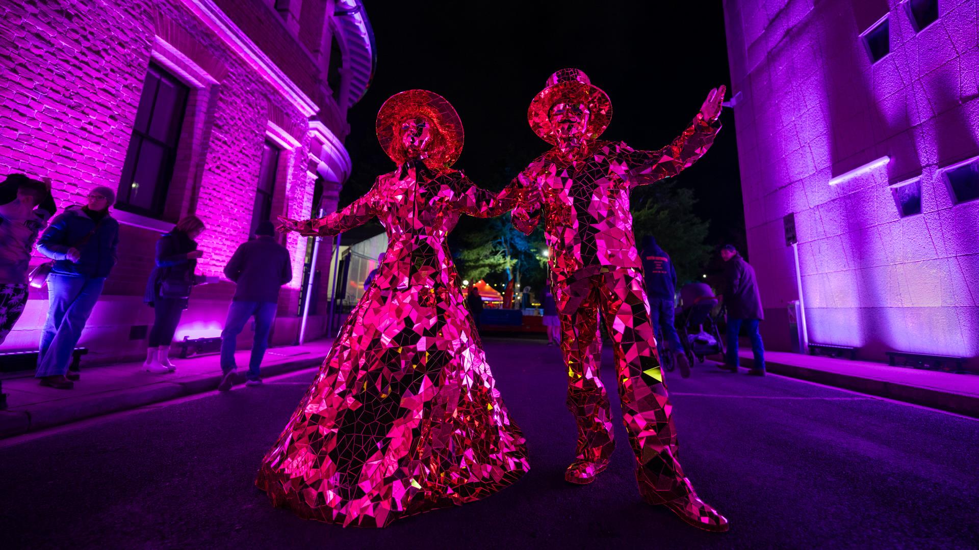 Two dress up characters dressed in reflective mirror outfits wandering through the lights at the festival.