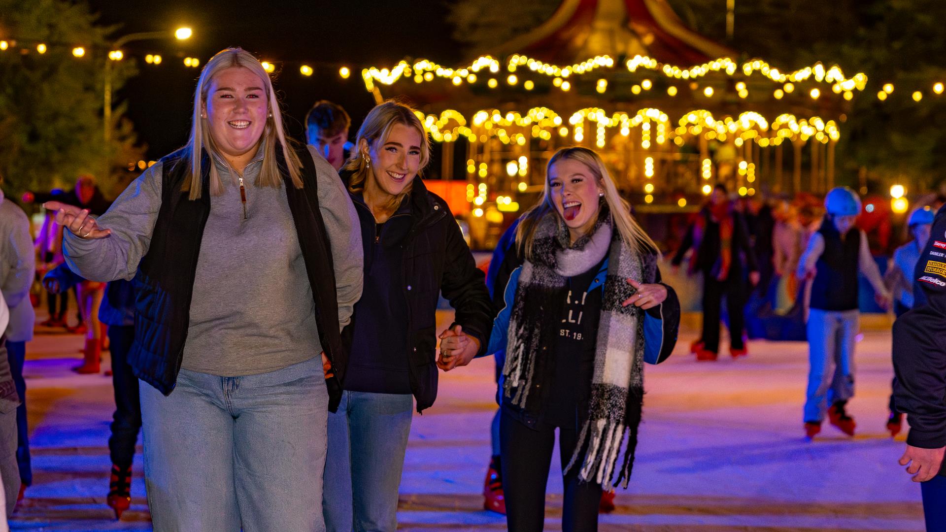 Three teenagers posing for the camera while ice skating at night.